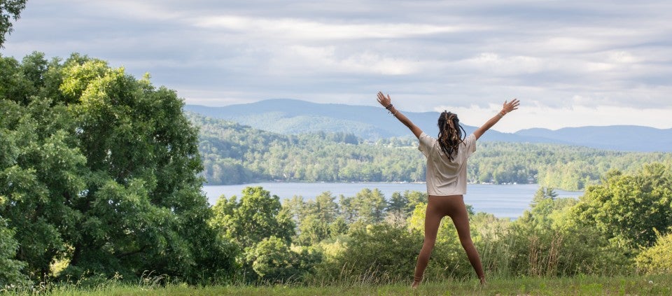 5 Practices for Easing the Transition into Daylight Saving Time Woman with hands raised facing a lake and mountains in the Spring.